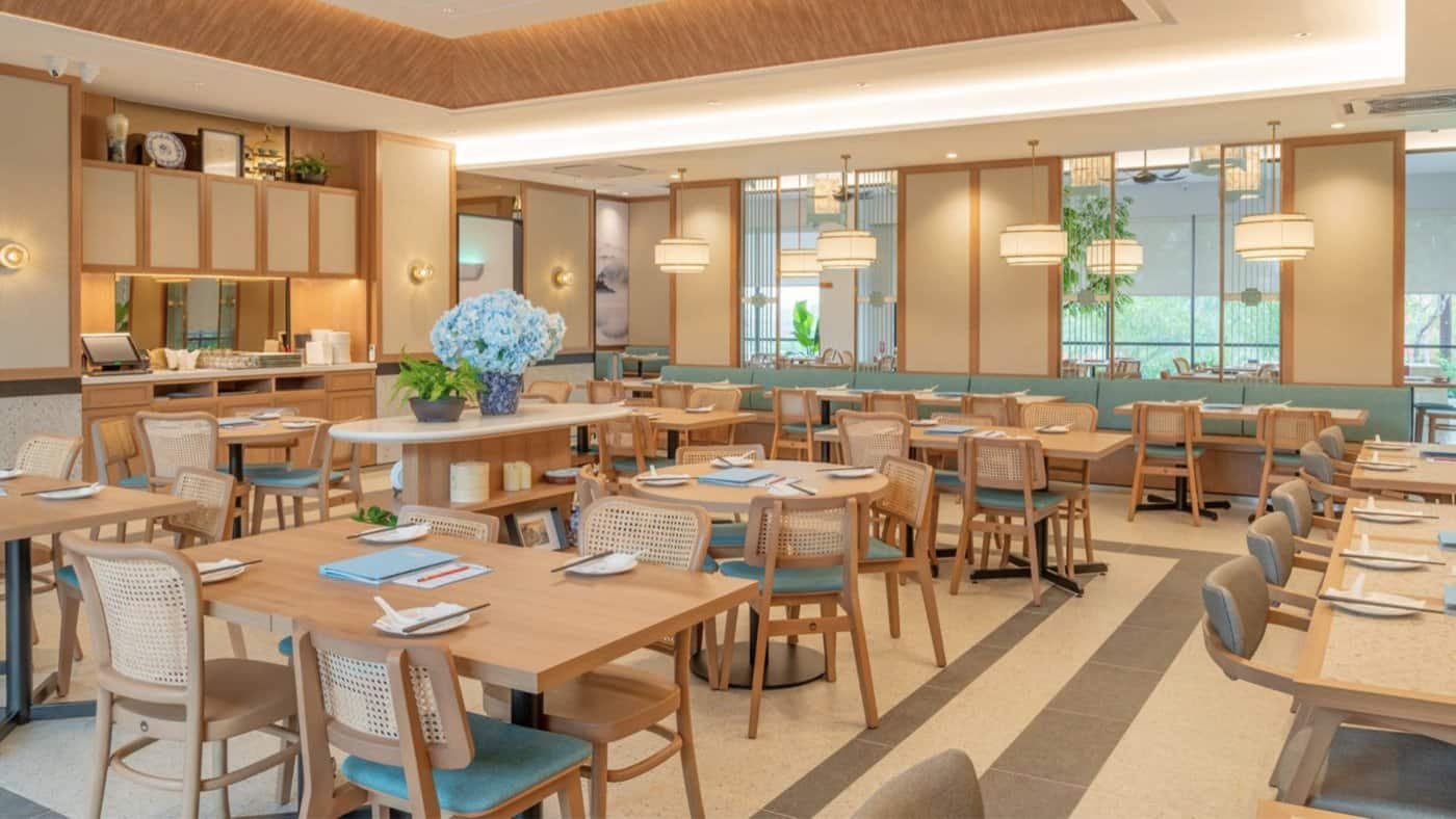 "Wide view of Dolly Dim Sum's interior in Elmina, Malaysia, highlighting neatly arranged dining tables with IKONS Furniture chairs, wooden decor accents, and soft, natural lighting."