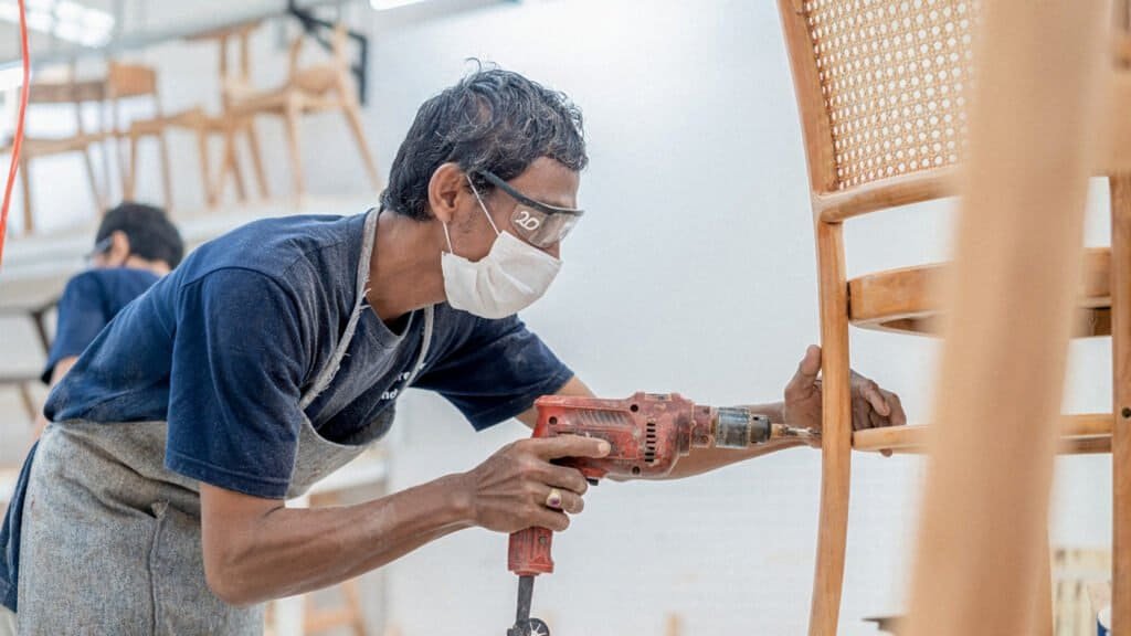 A craftsman at IKONS furniture factory in Semarang carefully sanding a chair frame, showcasing precision and attention to detail.