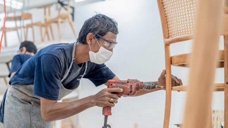 A craftsman at IKONS furniture factory in Semarang carefully sanding a chair frame, showcasing precision and attention to detail.